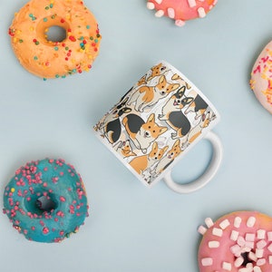 May include: White ceramic mug with a pattern of cartoon corgis in various poses. The corgis are brown, black, and white. The mug has a white handle.