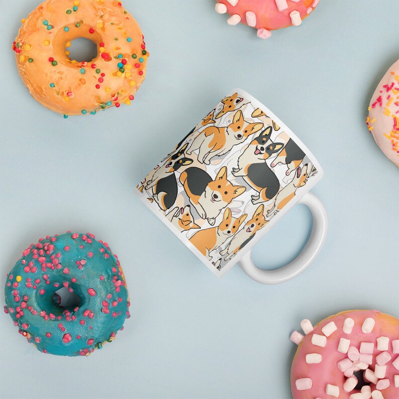 May include: White ceramic mug with a pattern of cartoon corgis in various poses. The corgis are brown, black, and white. The mug has a white handle.