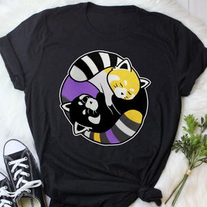 May include: Black t-shirt with a circular design of two stylized red pandas. One panda is black and white, the other is yellow and white. The design includes purple and yellow accents, and a white outline.