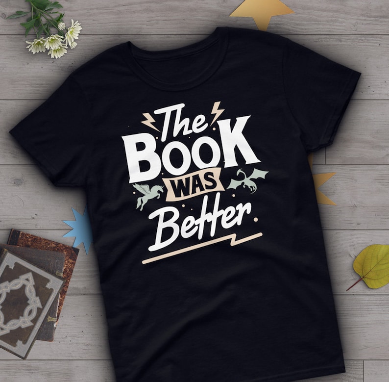 Pode incluir: Camiseta preta com texto branco que diz "The Book Was Better." O texto &eacute; estilizado com um raio e um gr&aacute;fico de unic&oacute;rnio e drag&atilde;o.