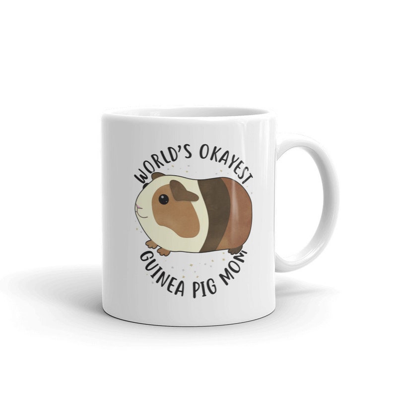 May include: White ceramic mug with a brown and white guinea pig illustration and the text "World's Okayest Guinea Pig Mom".