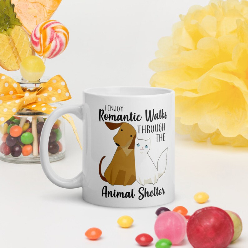May include: White ceramic mug with a black and white illustration of a dog and cat. The text on the mug reads "I enjoy romantic walks through the animal shelter."