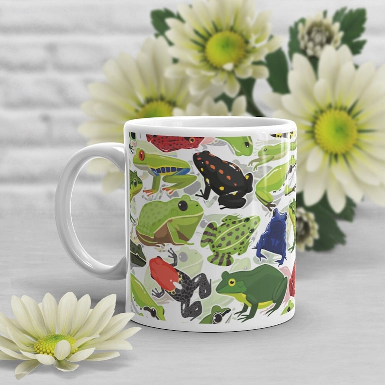 May include: White ceramic mug with a colorful pattern of frogs. The frogs are green, red, blue, and black. The mug has a white handle.