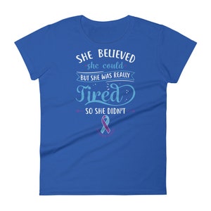 May include: A royal blue t-shirt with the text "She believed she could but she was really tired so she didn't" in white. A teal and purple ribbon is below the text.