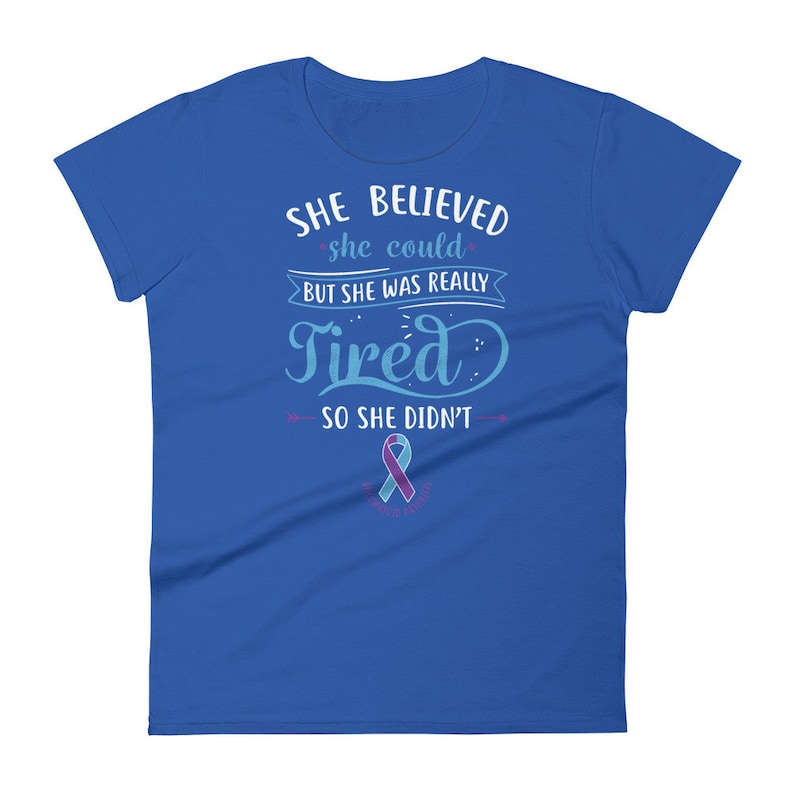 May include: A royal blue t-shirt with the text "She believed she could but she was really tired so she didn't" in white. A teal and purple ribbon is below the text.