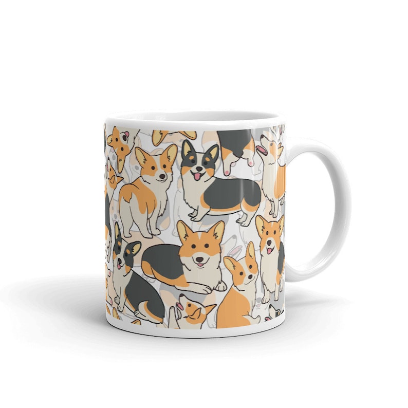 May include: White ceramic mug with a pattern of cartoon corgis in black, orange, and white. The corgis are in various poses, including sitting, standing, and lying down.