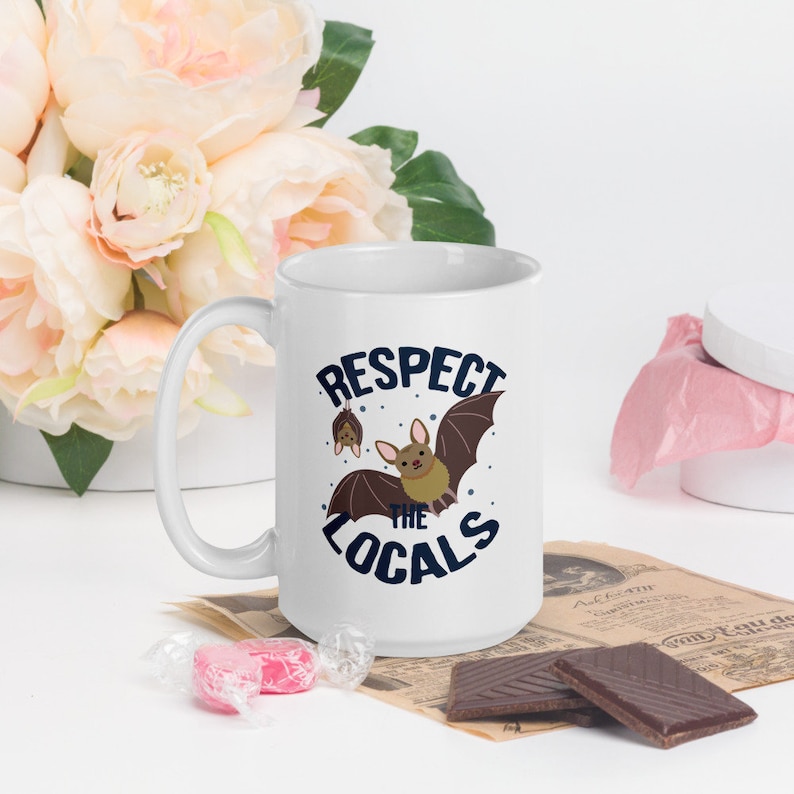 May include: White ceramic mug with a blue and brown graphic of bats and the text "Respect the Locals".