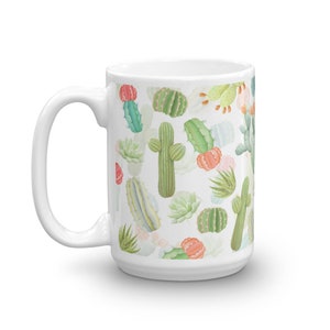 May include: White ceramic mug with a cactus pattern. The mug features a variety of cacti in different colors and sizes, including green, pink, and yellow. The cacti are arranged in a random pattern on the mug.