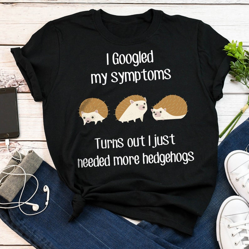 May include: Black t-shirt with white text that reads "I Googled my symptoms Turns out I just needed more hedgehogs". Three cartoon hedgehogs are pictured below the text.