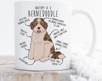 May include: White ceramic coffee mug with a brown and white Bernedoodle dog illustration. The mug features a humorous anatomical diagram of the dog with labels like "selective hearing device", "magical curly wavy cloud fluff", and "spring-loaded zooming sticks". The text "Anatomy of a Bernedoodle" is at the top of the mug.