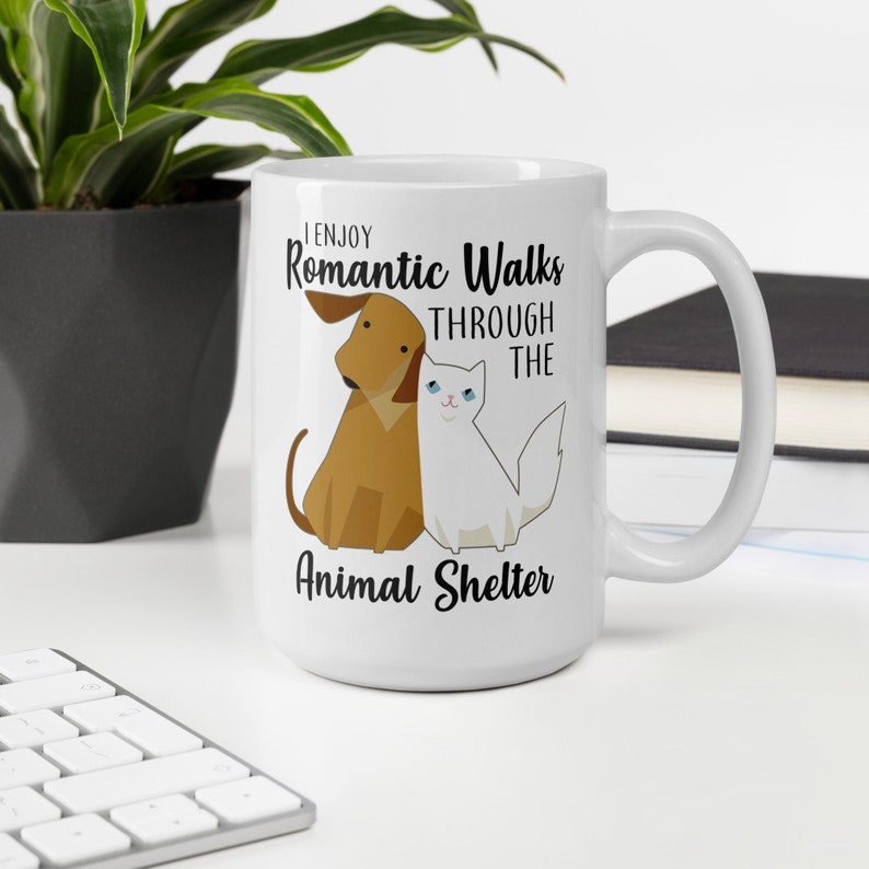 May include: White ceramic coffee mug with a black graphic of a dog and cat with the text "I enjoy romantic walks through the animal shelter".