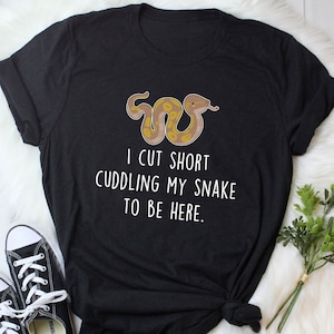 May include: Black t-shirt with a white graphic of a snake and the text "I cut short cuddling my snake to be here."