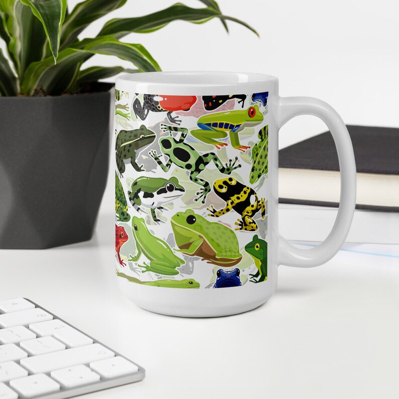 May include: White ceramic mug with a colorful pattern of frogs. The frogs are green, red, yellow, blue, and black. The mug has a large handle.