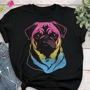 May include: Black t-shirt featuring a colorful graphic of a pug dog. The pug's face is rendered in a gradient of pink, yellow, and blue, with brown eyes and a black snout. The shirt is made of a soft material.