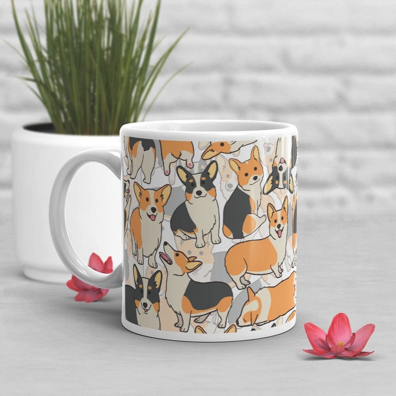 May include: White ceramic mug with a pattern of cartoon corgis in black, orange, and white. The corgis are in various poses, including sitting, standing, and running.