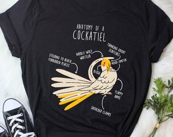 May include: Black t-shirt with a diagram of a cockatiel labeled "Anatomy of a Cockatiel." The diagram includes labels like "Nibbly Wolf Whistler" and "Flappy Arms." The shirt also features the text "Steering to Reach Forbidden Places."