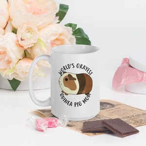 May include: White ceramic mug with a black and white illustration of a guinea pig and the text "World's Okayest Guinea Pig Mom".