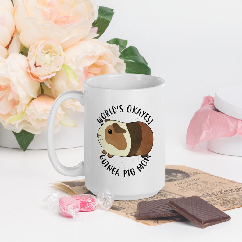 May include: White ceramic mug with a black and white illustration of a guinea pig and the text "World's Okayest Guinea Pig Mom".