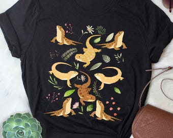 May include: Black t-shirt with a floral design and multiple images of bearded dragons. The bearded dragons are in various poses and are a light brown color.