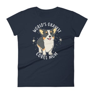 May include: Navy blue women's t-shirt with a white graphic of a corgi dog. The text "World's Okayest Corgi Mum" is printed on the shirt.