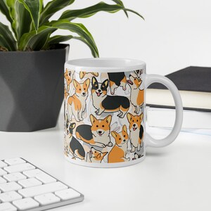 May include: White ceramic mug with a pattern of cartoon corgis in black, orange, and white. The corgis are in various poses, including sitting, standing, and running.
