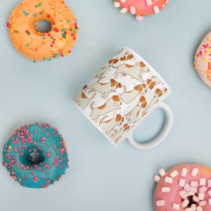 May include: White ceramic mug with a repeating pattern of brown and white Jack Russell terriers. The mug has a white handle and is surrounded by colorful donuts.
