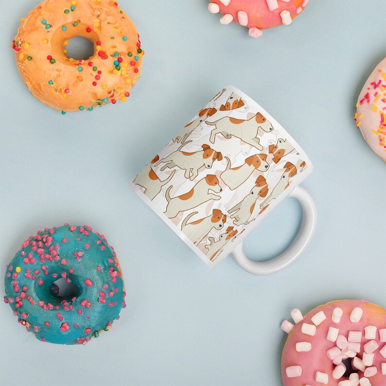 May include: White ceramic mug with a repeating pattern of brown and white Jack Russell terriers. The mug has a white handle and is surrounded by colorful donuts.