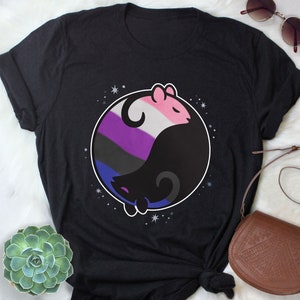 May include: Black t-shirt featuring a circular design with two stylized animal figures in a yin-yang composition. One figure is pink and white, the other black, with a genderqueer flag design. The design is surrounded by small white stars.