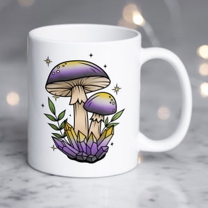 Puede incluir: Taza de cerámica blanca con un diseño de setas moradas y amarillas. Las setas están rodeadas de cristales morados y estrellas.