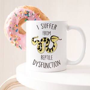 May include: White ceramic mug with a black and yellow snake illustration and the text "I suffer from reptile dysfunction".