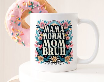 Peut inclure: Une tasse en céramique blanche avec un motif floral et le texte "Mama Mommy Mom Bruh" en lettres noires.