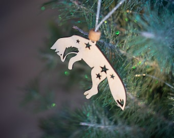 Può includere: Un ornamento di legno a forma di volpe con stelle ritagliate appeso a un albero di Natale verde.