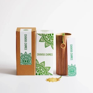 May include: A set of Chakra Chimes, including two boxes and a wooden chime holder. The boxes are brown and white with green mandala designs and the text "Chakra Chimes". The chime holder is cylindrical and made of wood.