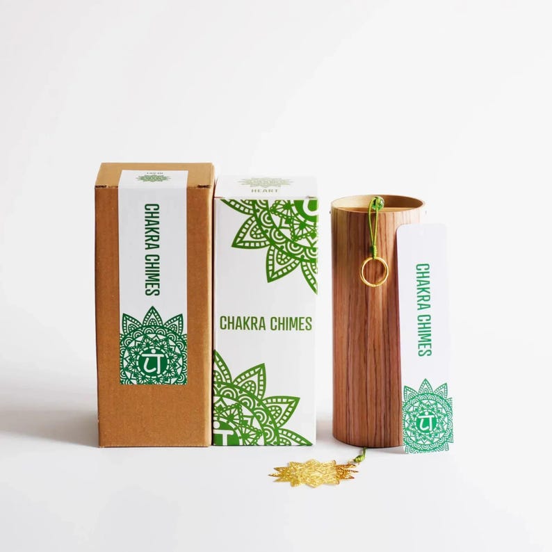 May include: A set of Chakra Chimes, including two boxes and a wooden chime holder. The boxes are brown and white with green mandala designs and the text "Chakra Chimes". The chime holder is cylindrical and made of wood.