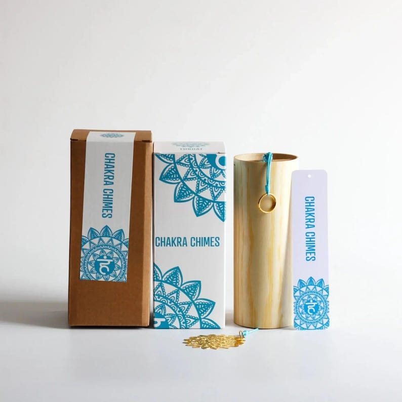May include: A set of Chakra Chimes, including a cylindrical wooden chime, two boxes, and a tag. The boxes and tag feature a teal mandala design and the words "Chakra Chimes". A gold-colored decorative element is at the base.
