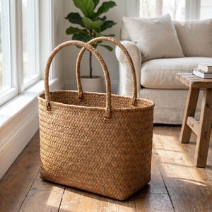 May include: A rectangular woven basket with two braided handles. The basket is made of light brown material and has a textured surface. The handles are arched and attached to the top of the basket.