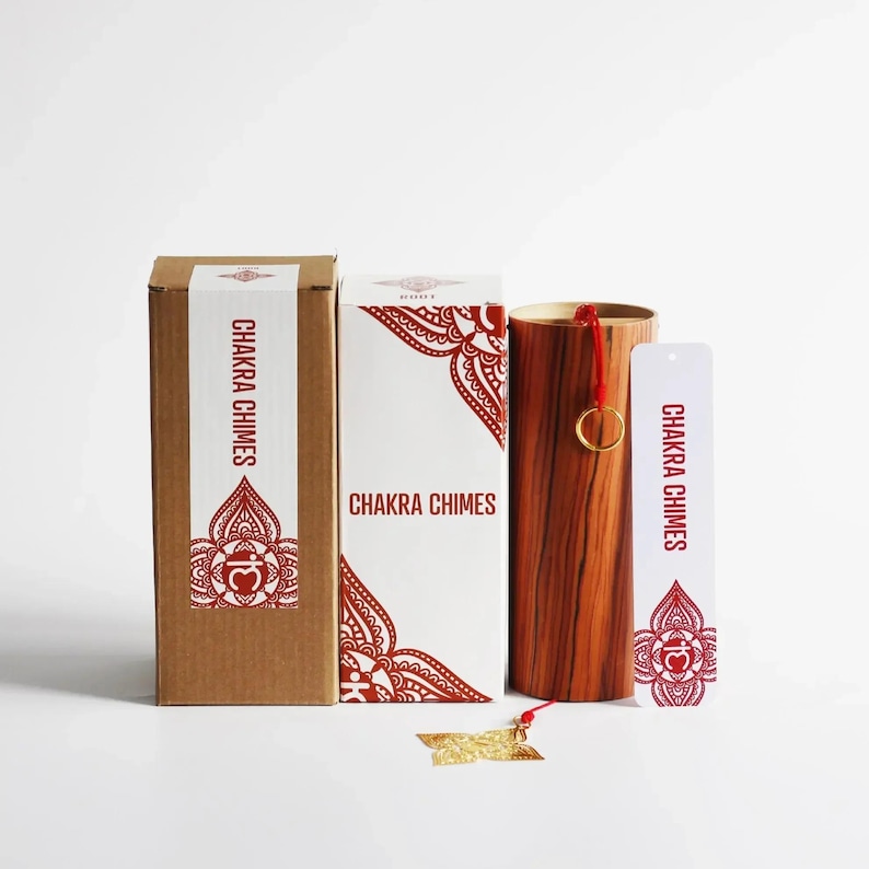 May include: A set of Chakra Chimes, including a wooden chime, two boxes, and a bookmark. The boxes and bookmark feature the text "Chakra Chimes" in red. The chime is cylindrical with a gold ring and red cord.