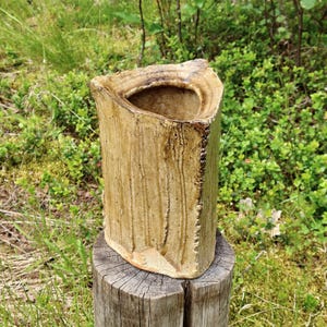 May include: A triangular ceramic vase with a textured, tan-coloured exterior featuring vertical drip patterns and a rough, uneven rim. The vessel has a hollow centre and a weathered, earthy appearance with visible clay variations across its surface.