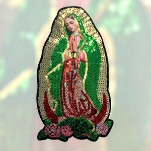 May include: A sequined patch featuring a religious figure in a green and red robe, with a gold halo. The figure is depicted with hands clasped in prayer. The patch is outlined in black and has a floral design at the bottom.