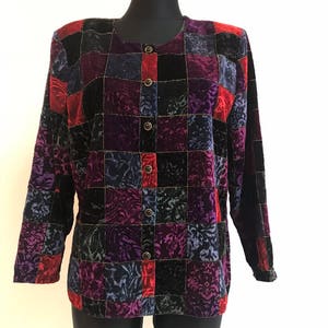 Peut inclure: Une blouse à manches longues boutonnée avec un motif patchwork. Le tissu est un mélange de velours et de tissu à motifs dans les tons noir, rouge, violet et bleu.