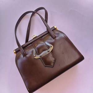 May include: A brown leather handbag with a gold clasp and a metal handle. The bag has a vintage style.