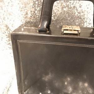 May include: A brown leather briefcase with a handle and a gold lock. The briefcase has white mould spots on the surface.