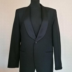 Peut inclure: Une veste de smoking noire avec un col châle en satin. La veste a une fermeture à bouton unique et deux poches.