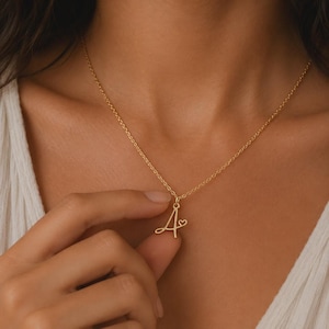 Peut inclure: Un collier doré composé d'une chaîne fine et d'un pendentif en forme de lettre A cursive, intégrant un petit cœur sur le côté droit de la lettre. Le pendentif est suspendu à la chaîne par un anneau de jonction simple et discret.