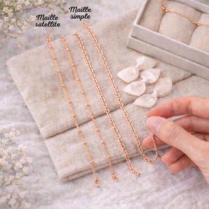 May include: Four rose gold chain bracelets displayed on a neutral linen surface. Two bracelets are labeled "Maille satellite" and feature small beads. The other two are labeled "Maille simple" and have a classic chain link design. A hand holds one of the bracelets.