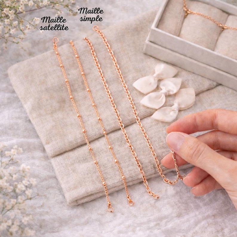 May include: Four rose gold chain bracelets displayed on a neutral linen surface. Two bracelets are labeled "Maille satellite" and feature small beads. The other two are labeled "Maille simple" and have a classic chain link design. A hand holds one of the bracelets.