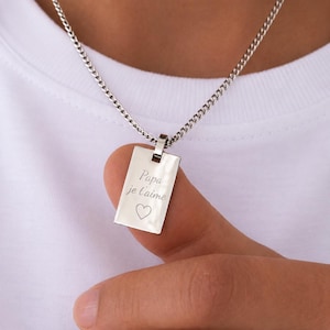 Könnte beinhalten: Eine silberfarbene rechteckige Anhängerkette mit polierter Metalloberfläche. Der Anhänger ist mit dem Text Papa je t'aime und einem kleinen Herzsymbol graviert. Das Schmuckstück hängt an einer passenden silberfarbenen Panzerkette.