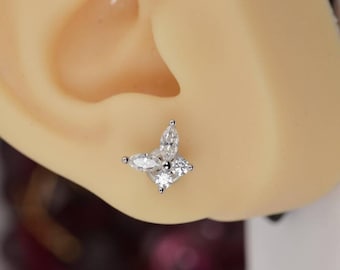 May include: A silver stud earring with a floral design is shown in close-up. The earring has four clear, sparkling gemstones arranged in a flower shape. The earring is set against a light skin tone.