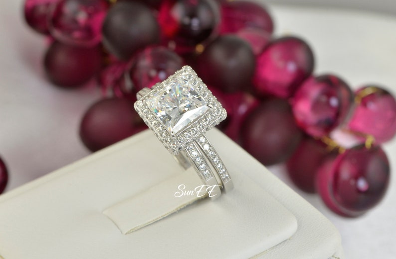 May include: A silver engagement ring set with a large square-cut cubic zirconia stone surrounded by smaller stones. The ring is on a white display stand.