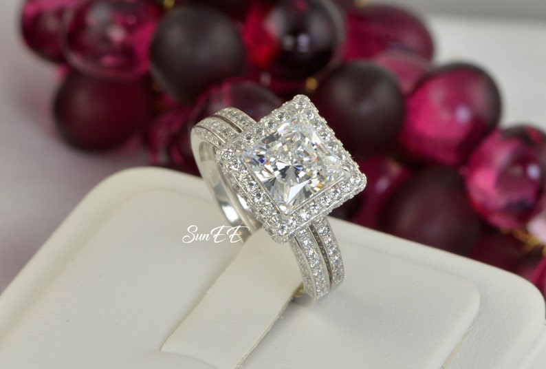 May include: A silver engagement ring set with a large, square-cut diamond surrounded by smaller diamonds. The ring is on a white display stand.